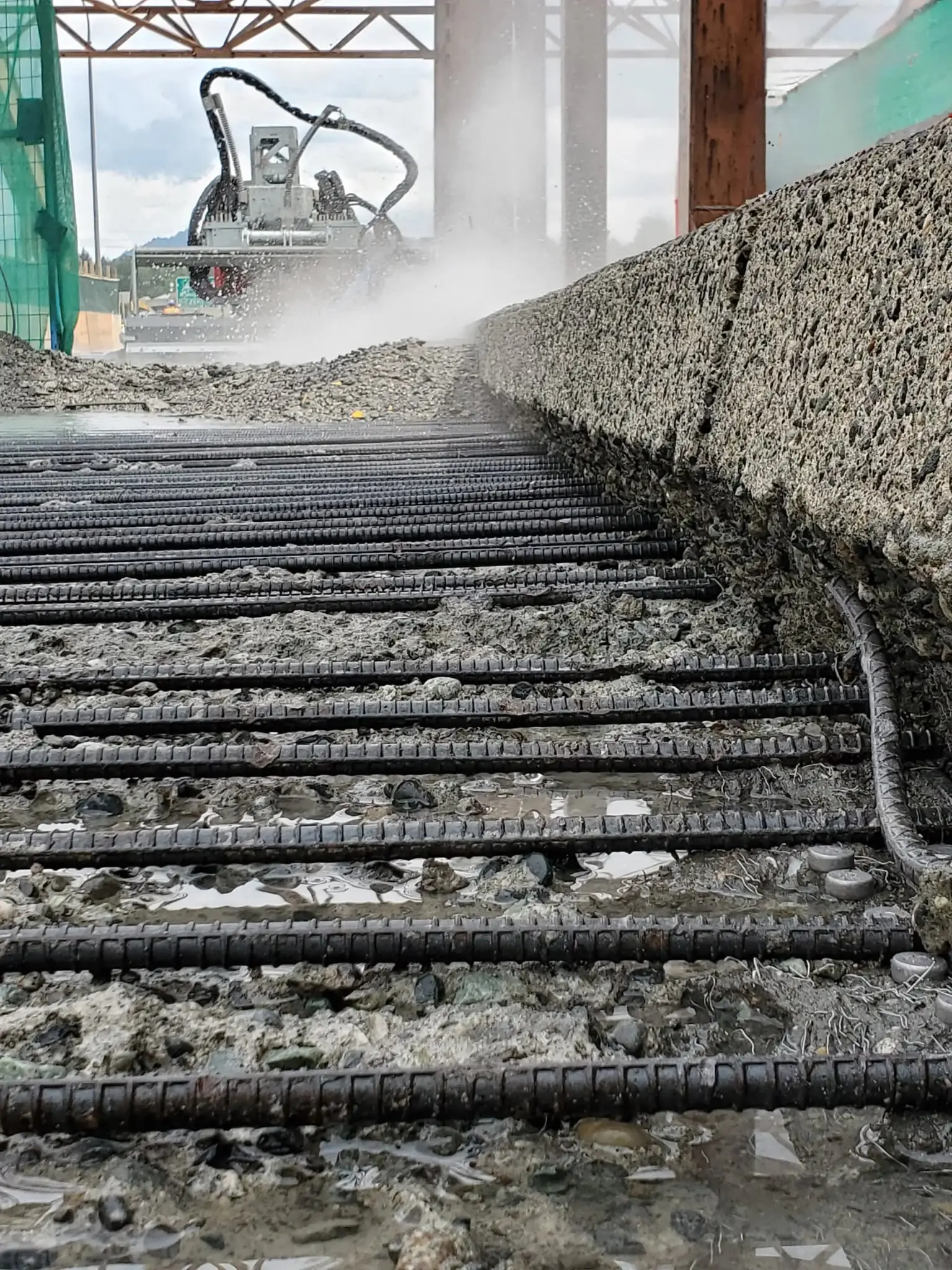Hydrodemolition-robot nedbryder beton på et dæk, hvor armeringsnettet ligger frilagt i forgrunden.